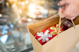 Male hand holding paper shopping bag with red gift boxes inside at Christmas event in department store. Buying present for Xmas holiday and New Year celebration concept