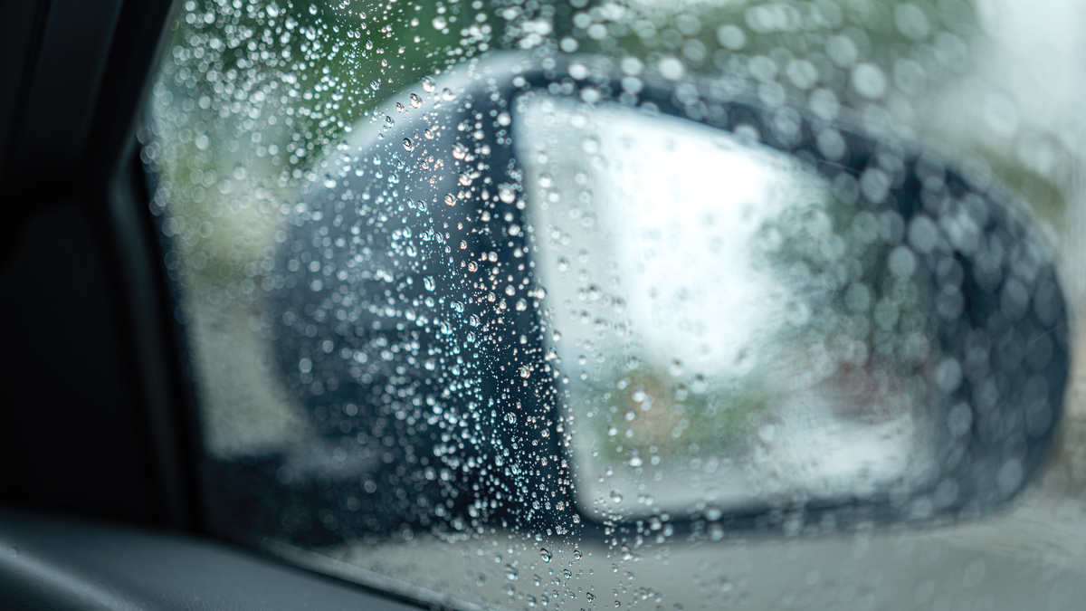 Water or rainy droplet on car side glass with side mirror and rearview as background. Transportation in raining season scene, close-up with selective focus.