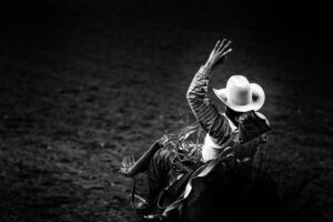 Monochrome rodeo cowboy in a white hat riding a bronco in ththe